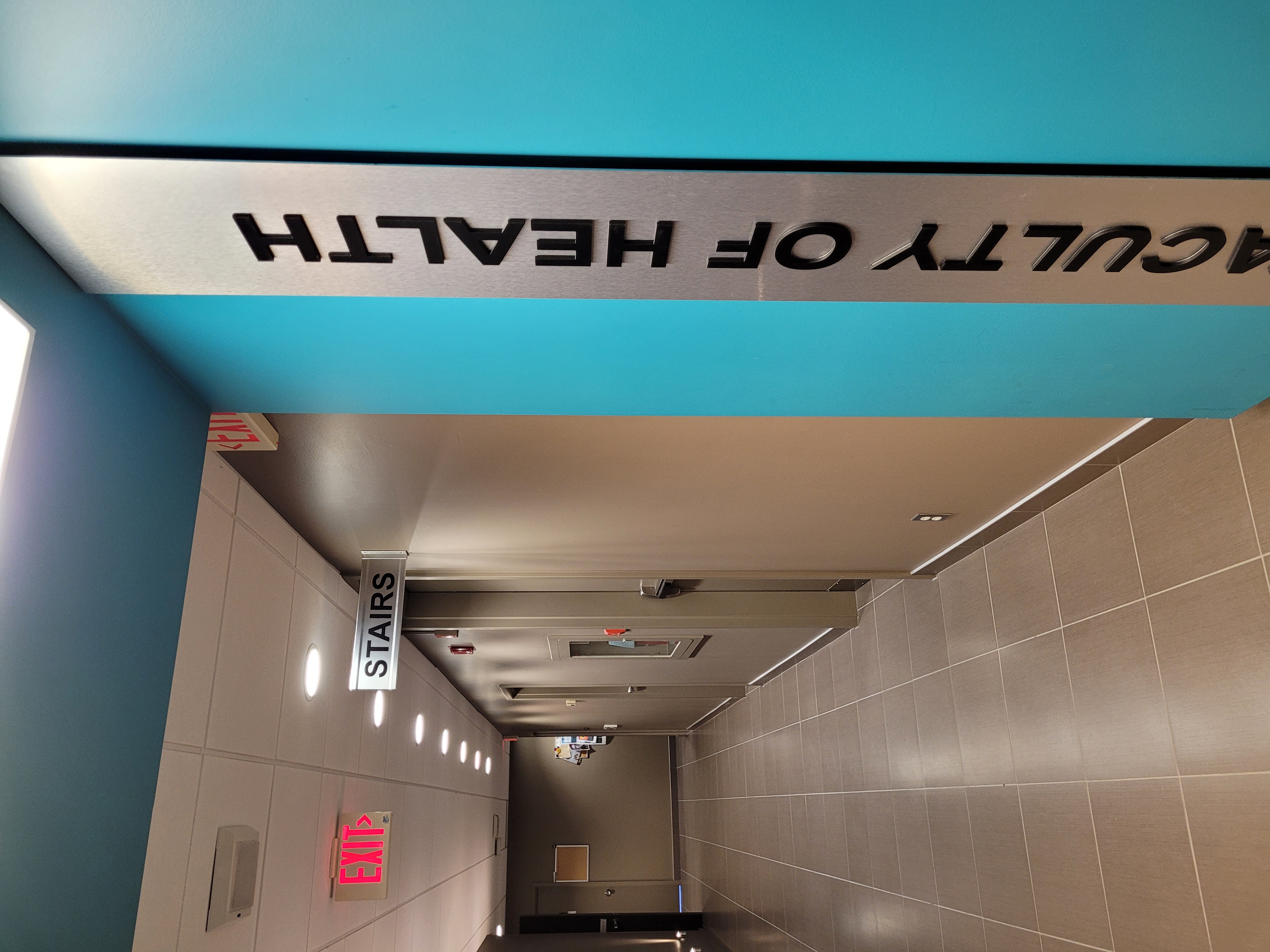 Hallway with a blue wall on the right side. There is a sign on the blue wall that says Faculty of Health.